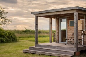 A wooden structure with a glass door, a small outdoor seating area, and a grassy field in the background. - Holiday apartment with 2 bedrooms (Loddin)