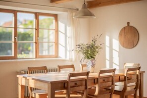 A dining area with a wooden table and chairs, a vase with flowers, and a window with curtains. - Holiday apartment with 2 bedrooms (Loddin)