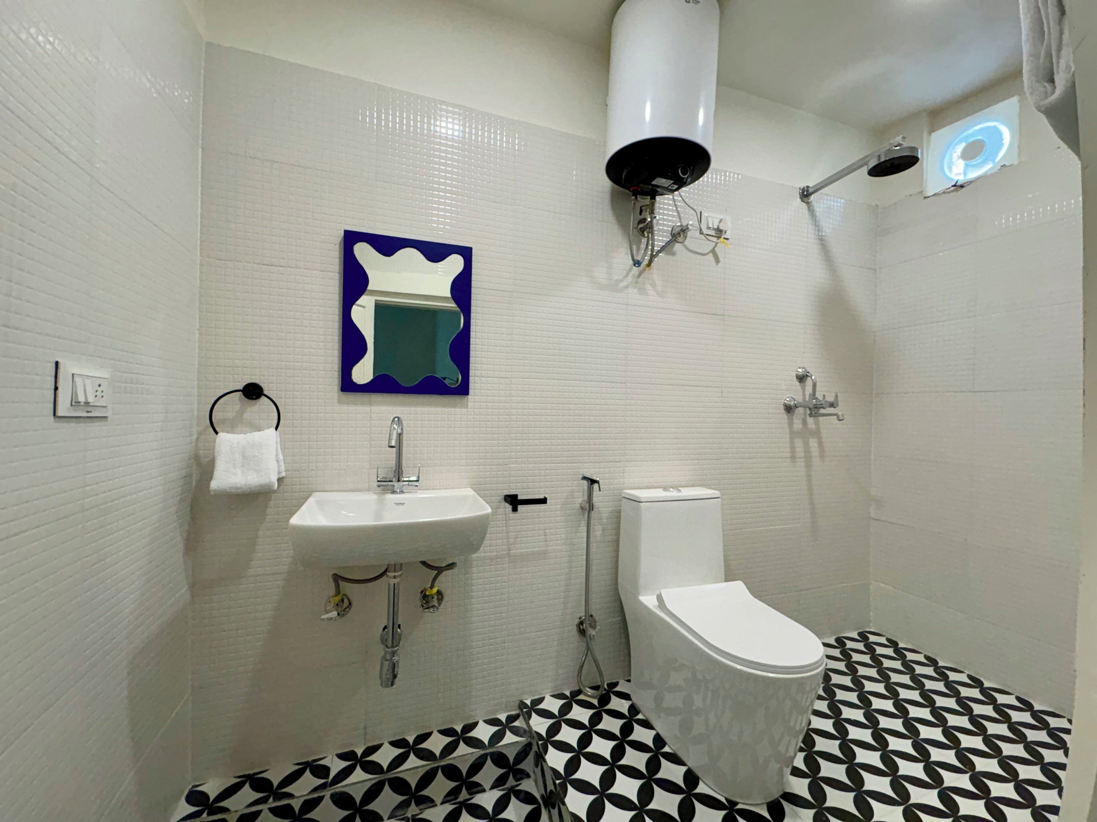 A bathroom with a white sink, toilet, and shower. There is a blue and white mirror above the sink and a white towel hanging on a rack.