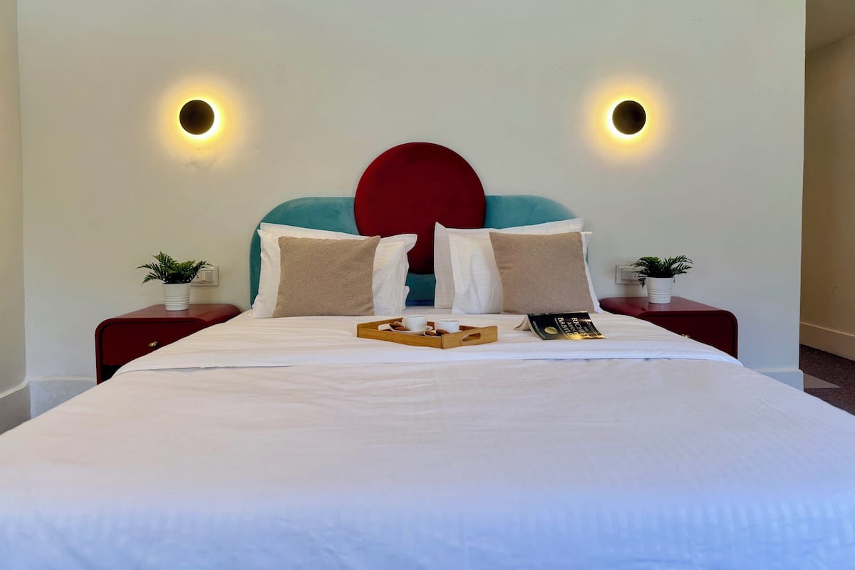 A neatly made bed with pillows, a tray with a cup and a book, and two wall-mounted lights.