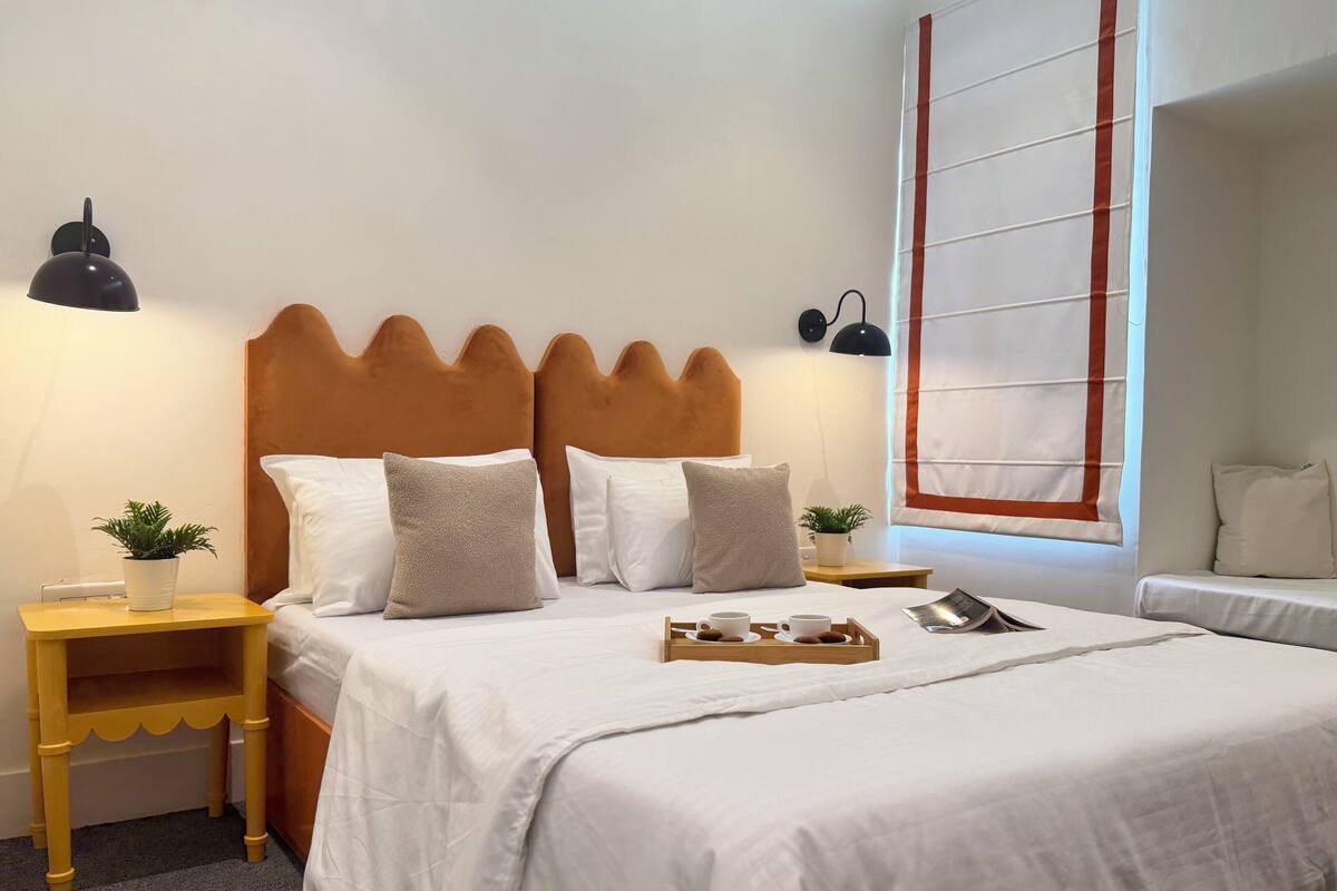 A neatly made bed with white bedding, a wooden headboard, and a bedside table with a plant.