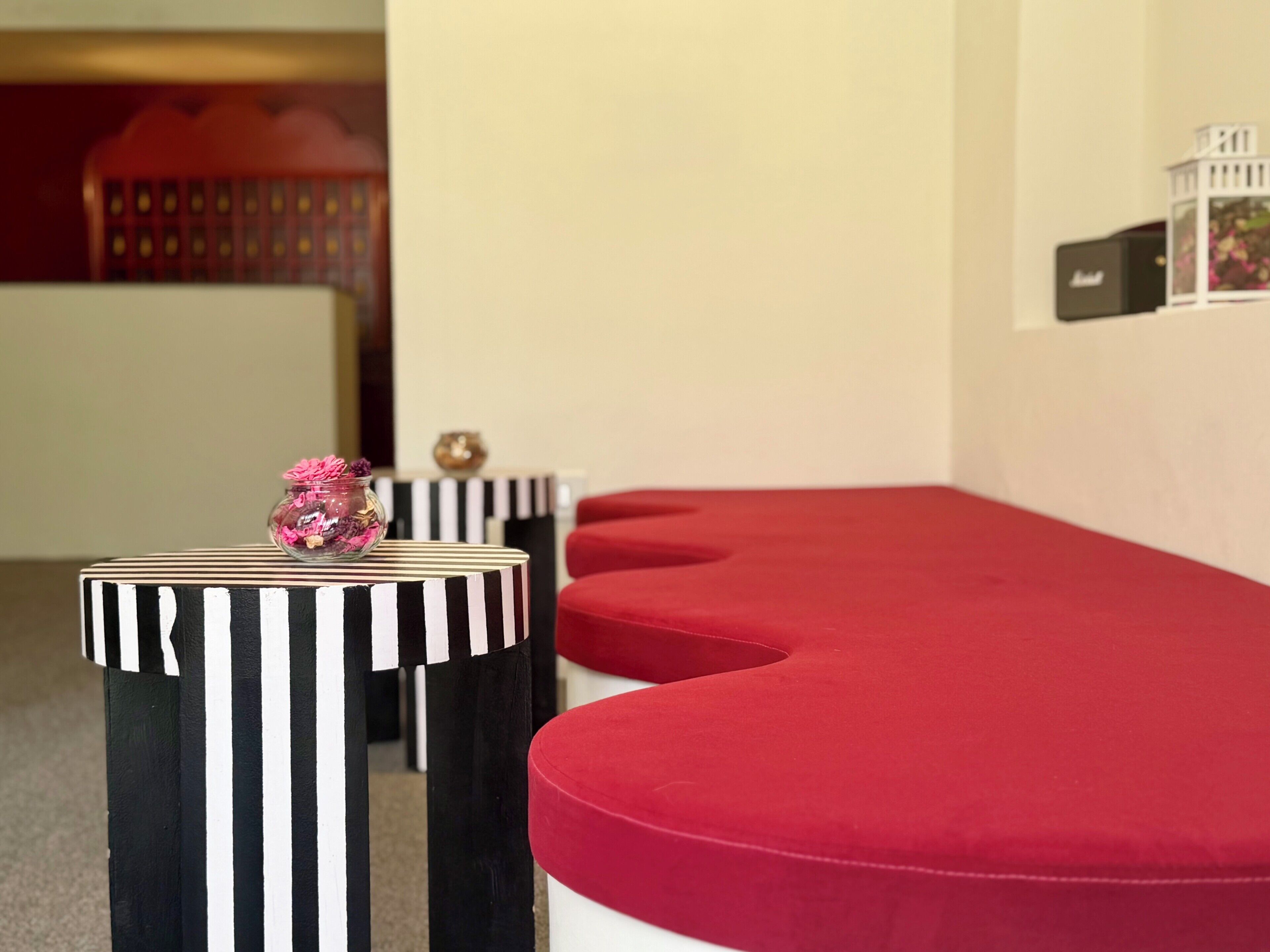 A room with a red cushioned bench, a striped table with a glass jar, and a black and white striped table.
