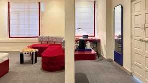 A room with a red sofa, a small table with a tray, a laptop on a desk, and a door with a blue frame. - NauKothi Jaipur (Jaipur)