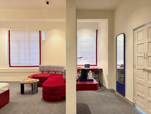 Een kamer met een rode bank, een klein tafeltje met dienblad, een laptop op een bureau en een deur met een blauwe omlijsting.