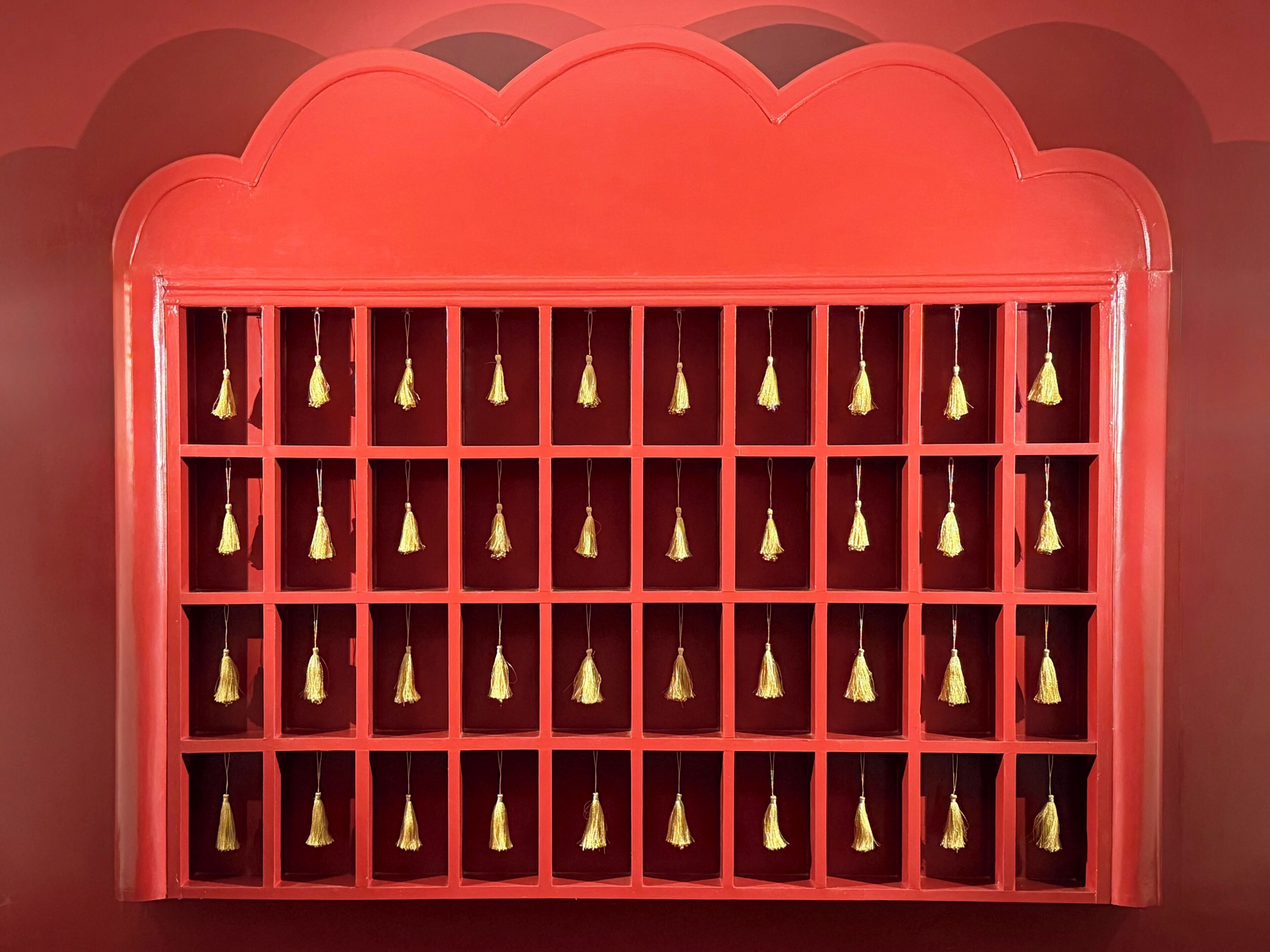 A red display case with multiple compartments, each containing a golden tassel.