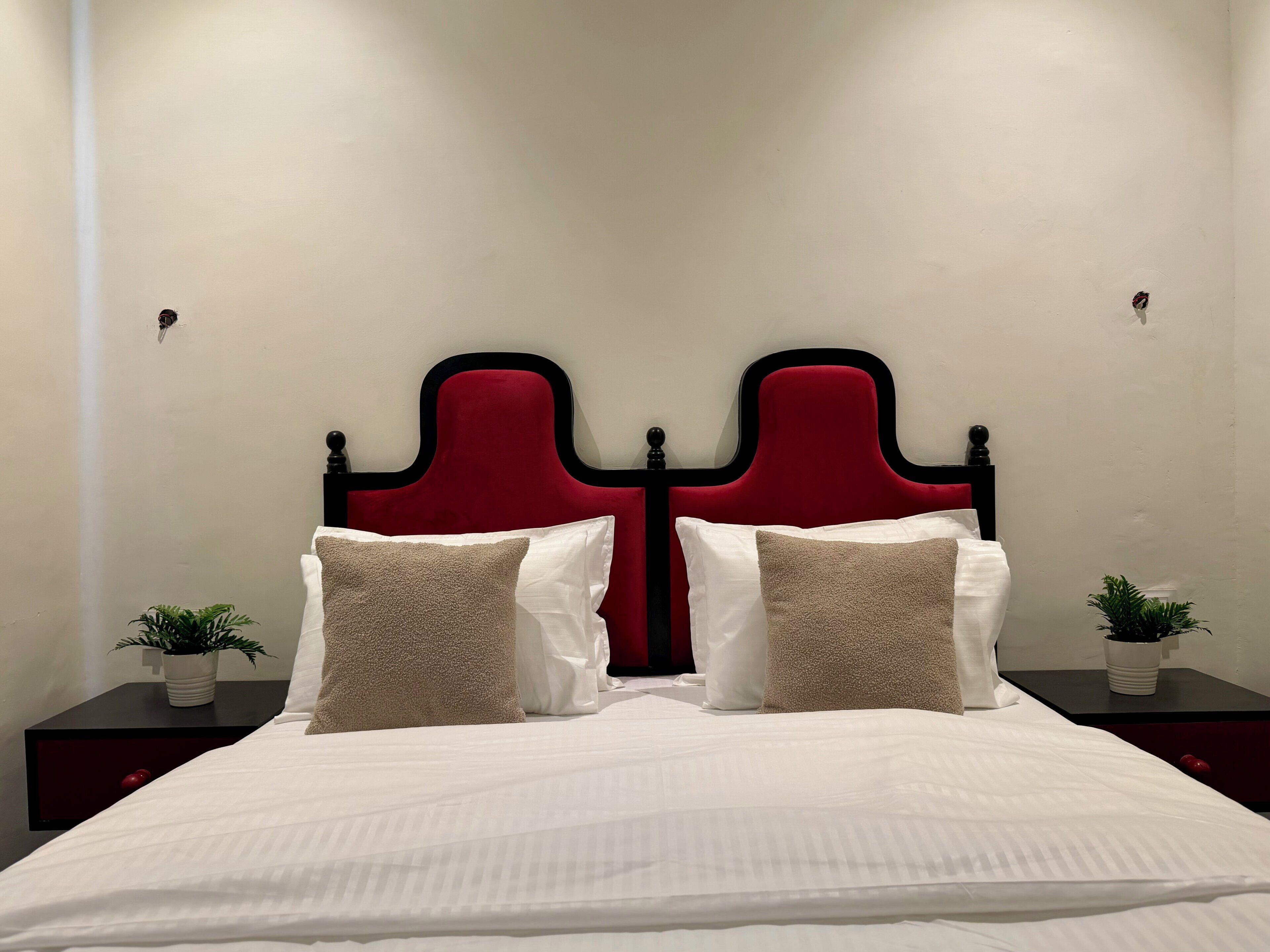 A bed with a red headboard, white bedding, and two bedside tables with potted plants.