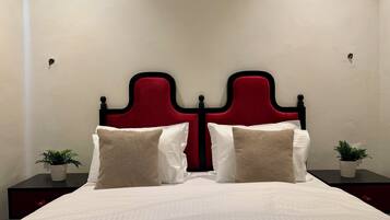 Una cama con cabecera roja, ropa de cama blanca y dos mesitas de noche con plantas en macetas.