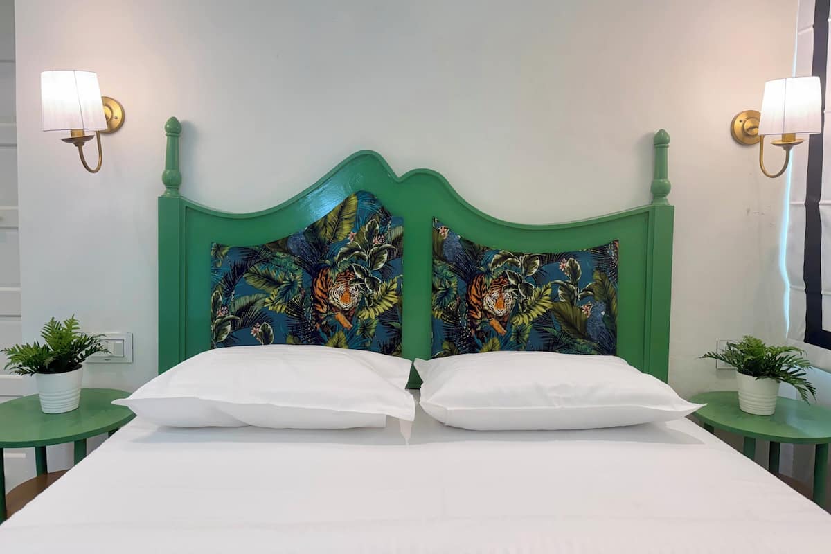A bed with white linens, two green nightstands with potted plants, and a headboard with a tropical print.