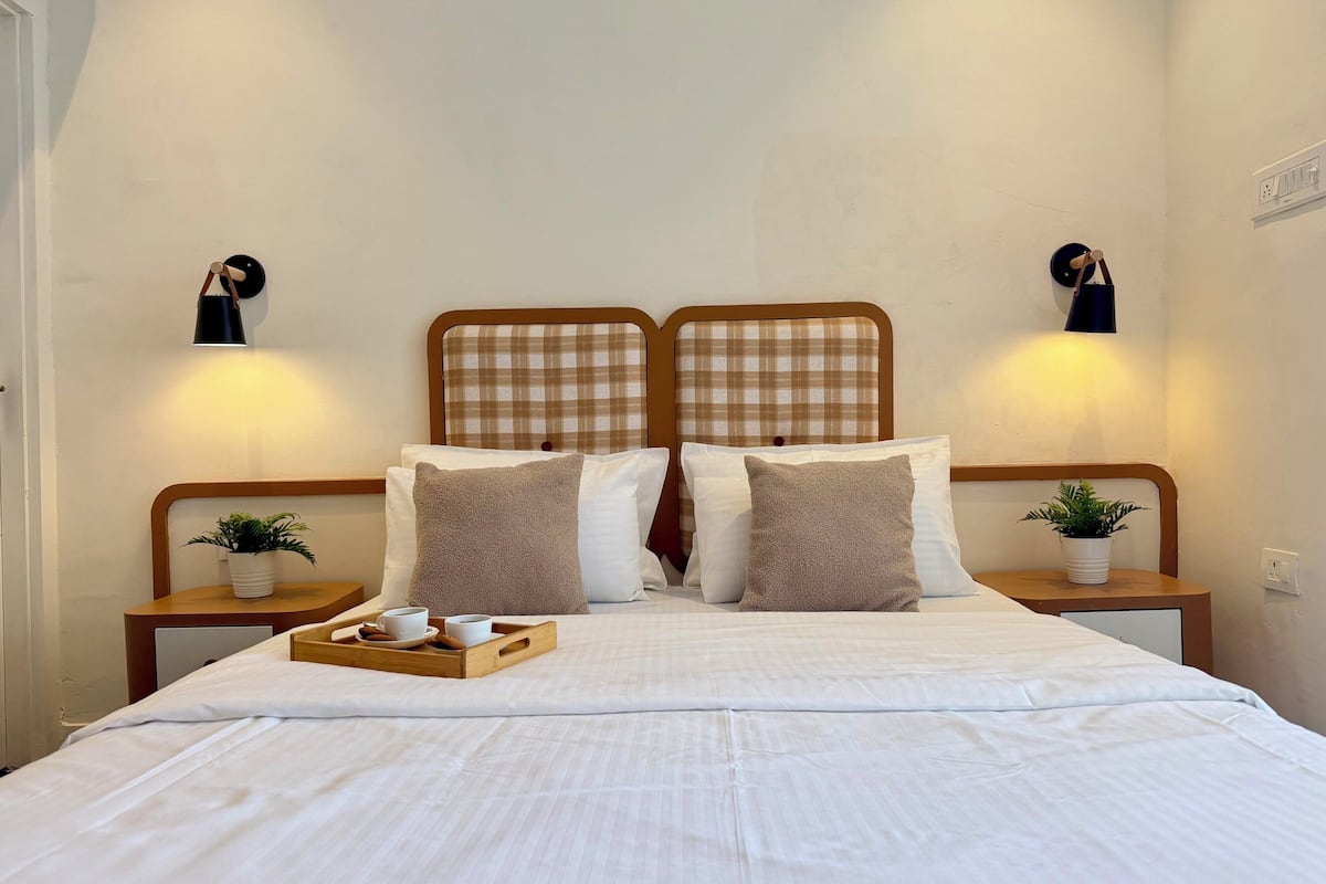 A bed with a checkered headboard, two bedside tables with lamps, a tray with cups and a bowl, and a small plant on each table.