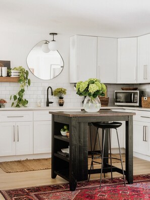 A kitchen with white cabinets, a wooden island, a round mirror, and a microwave. - Caviar on Pine in Downtown McKinney • Sleeps 9 • Luxe Stay • Elevated Coffee Bar (McKinney)