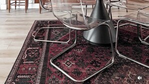 Un'area pranzo moderna con un tavolo rotondo, sedie trasparenti, un tappeto decorato e una lampada a sospensione.