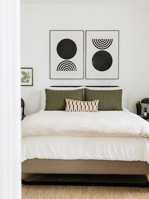A bed with a white duvet and green pillows, a black frame, and a picture of abstract art on the wall. - Caviar on Pine in Downtown McKinney • Sleeps 9 • Luxe Stay • Elevated Coffee Bar (McKinney)