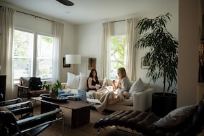 A living room with two sofas, a coffee table, a potted plant, and a window with curtains. - Caviar on Pine in Downtown McKinney • Sleeps 9 • Luxe Stay • Elevated Coffee Bar (McKinney)