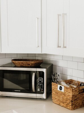 Une cuisine équipée d’un four à micro-ondes de la marque Farberware, de meubles blancs et d’un panier en osier contenant des ustensiles de cuisine.
