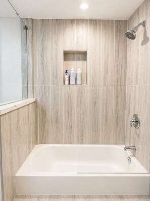 Ein modernes Badezimmer mit einer freistehenden Badewanne, einer Duschbrause und einem Ablagefach für Toilettenartikel.