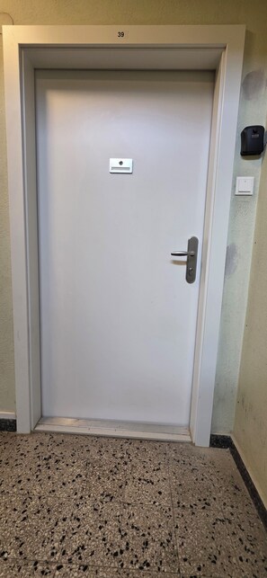 A closed door with a keypad lock, a small label above it, and a light switch on the wall to the right.