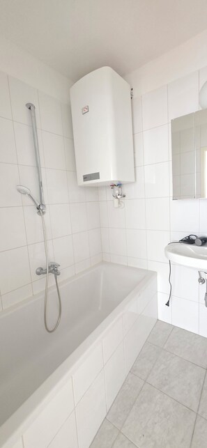A bathroom with a bathtub, a shower, a white tiled wall, and a sink with a mirror.