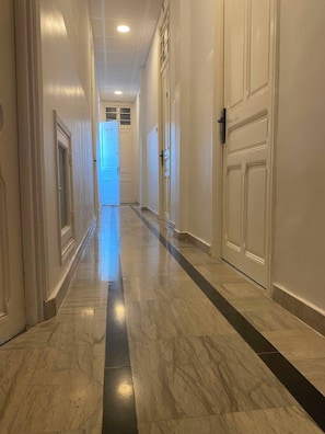 Un pasillo con piso de mármol, puertas blancas e iluminación empotrada en el techo.