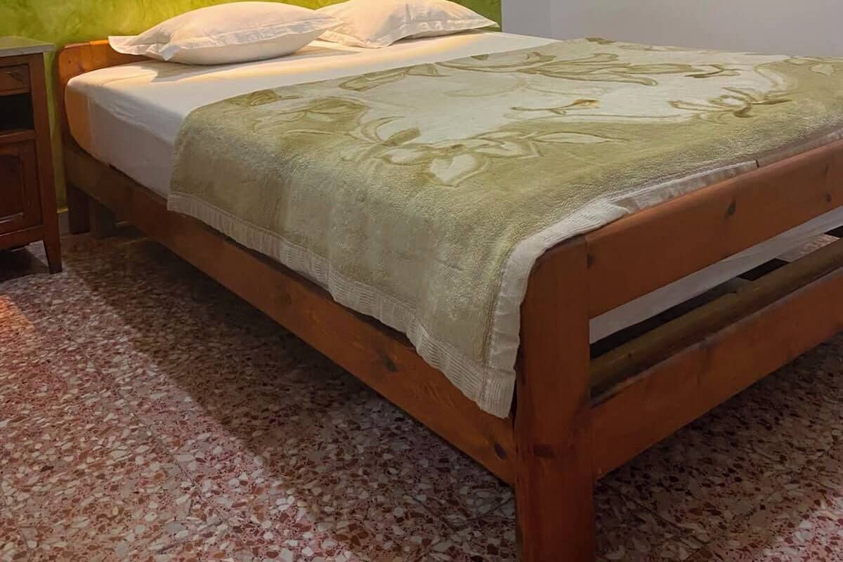 A single bed with a wooden frame, a green textured wall, and a nightstand with a lamp.