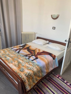 Una cama individual con una colcha estampada, una lámpara de pared y un radiador.