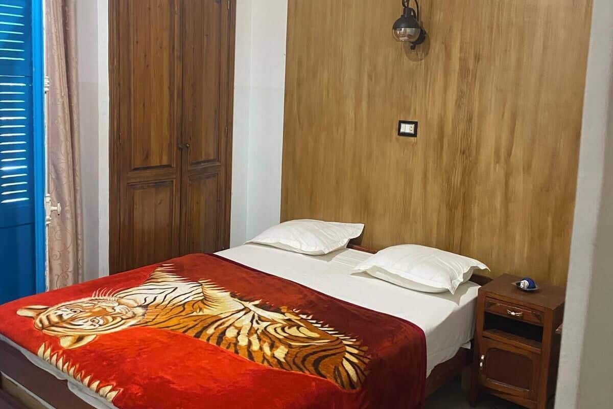 A bedroom with a bed, a wooden wardrobe, a nightstand, and a wall-mounted light fixture.