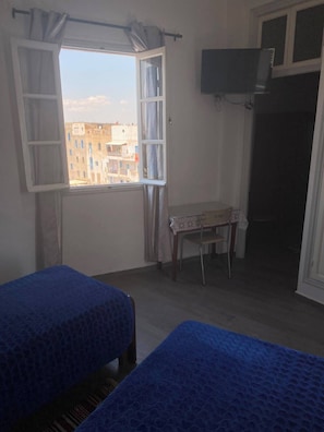Una habitación con dos camas, una mesa con mantel estampado, un televisor montado en la pared y una ventana con cortinas.