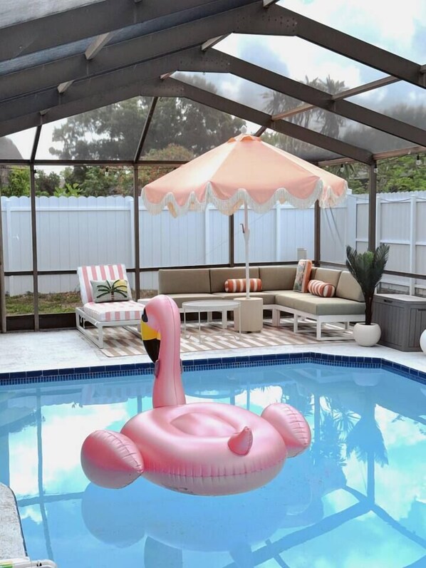 Une piscine extérieure couverte, agrémentée d’un flotteur en forme de flamant rose, de chaises longues et d’un auvent.