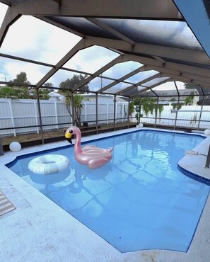 Une piscine agrémentée d’un flotteur en forme de flamant rose et d’un autre en forme d’anneau, le tout entouré d’une zone abritée par un toit en métal.