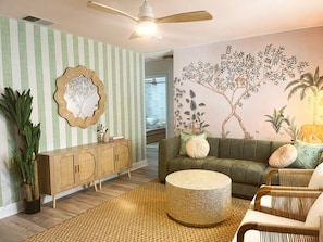 Ein Wohnzimmer mit gestreifter Wand, einem Rattan-Sofa, einem runden Couchtisch, einem Schrank und einem Deckenventilator.