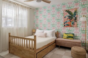 A bedroom with a wooden bed, a bedside table, a lamp, and a wall with a tropical pattern. - Palm Royale Pool Oasis •10m DT St Pete •15m Beach (St. Petersburg)