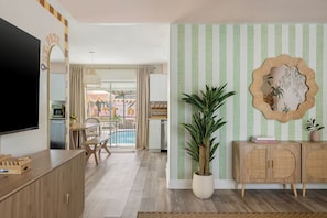 A modern living room with a flat-screen TV, a dining area with a pool view, and a green-striped wall with a decorative mirror. - Palm Royale Pool Oasis •10m DT St Pete •15m Beach (St. Petersburg)