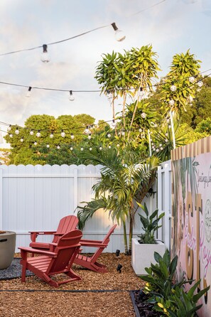 A patio area with red Adirondack chairs, a white picket fence, and string lights. - Palm Royale Pool Oasis •10m DT St Pete •15m Beach (St. Petersburg)