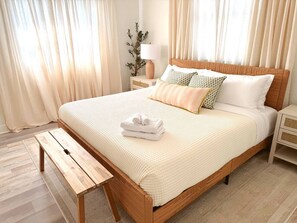 Un lit bien fait, avec une tête de lit en bois, une table de chevet et un banc.