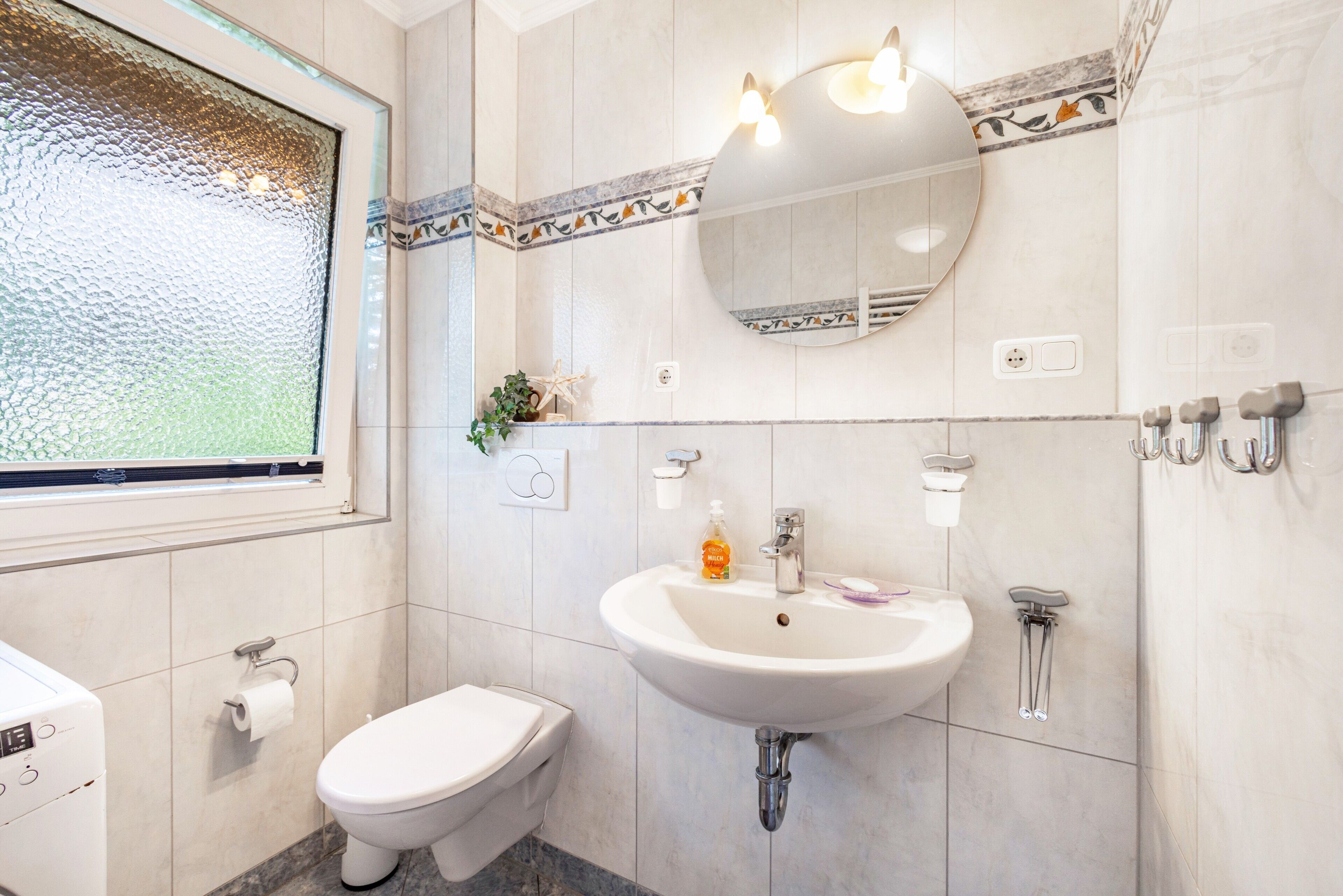 A bathroom with a toilet, sink, mirror, and window.