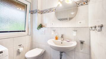 A bathroom with a toilet, sink, mirror, and window.