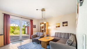 En moderne stue med sofa, lænestole, et sofabord og et spisebord. Der er en skydedør af glas, der fører ud til en have.