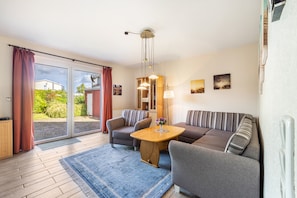 A modern living room with a sofa, armchairs, a coffee table, and a dining table. There is a sliding glass door leading to a garden. - Holiday Apartment for 5 People (80 m²) in Dahme (Dahme)