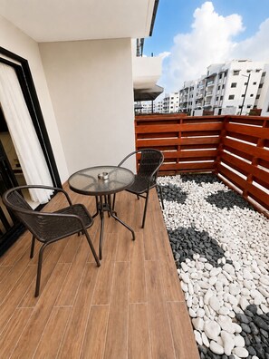 Eine Terrasse im Freien mit einem runden Glastisch und zwei Korbstühlen, umgeben von einem Holzzaun und Kies.