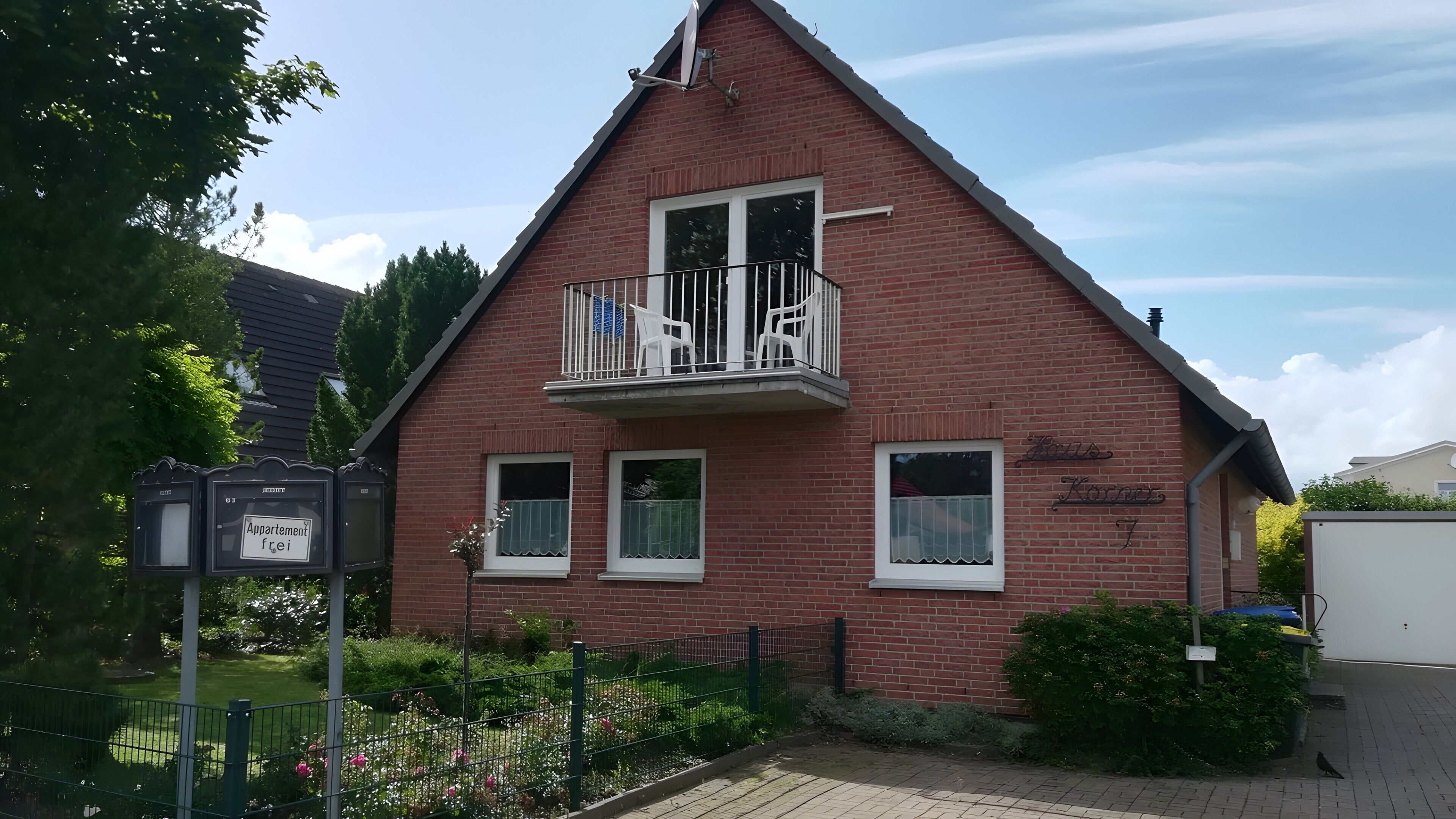 A red brick building with a balcony, a sign reading 'Appartement frei,' and a small garden area.. Holiday Apartment for 5 People (55 m²) in Dahme