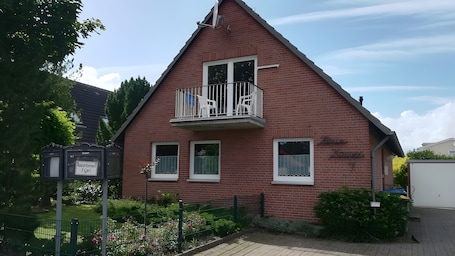 A red brick building with a balcony, a sign reading 'Appartement frei,' and a small garden area.. Holiday Apartment for 5 People (55 m²) in Dahme