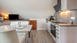 Een moderne keuken met witte kastjes, een eettafel gedekt voor twee personen, en een flatscreen televisie aan de muur.