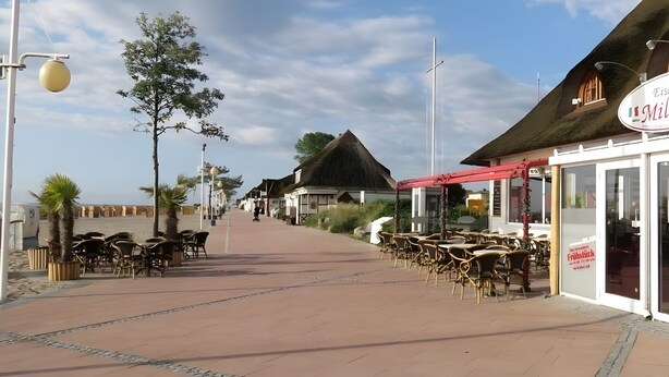 Een kustpad met gebouwen met rieten daken, buiten zitplaatsen en een heldere lucht.