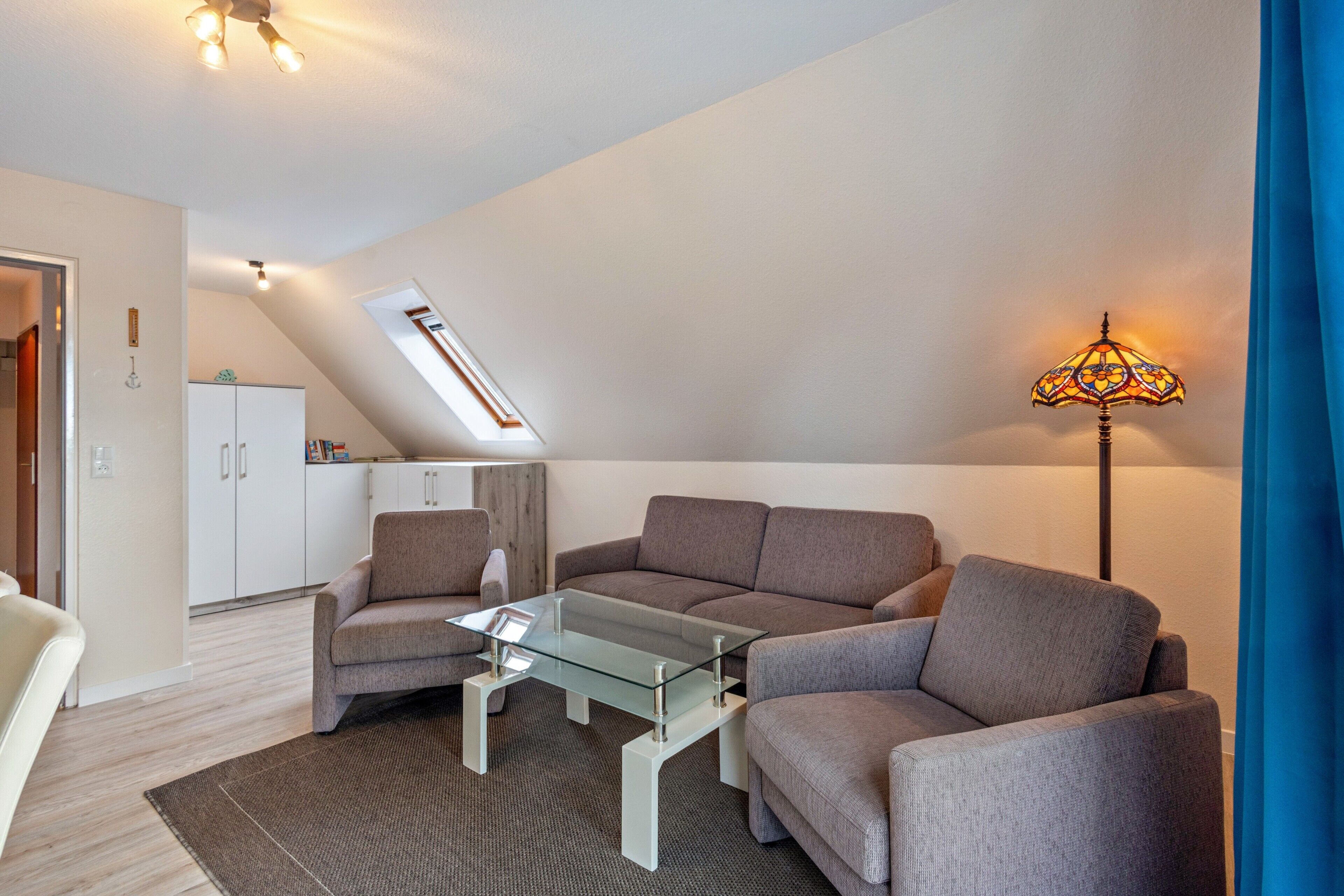 A modern living room with a glass coffee table, grey sofas, a lamp, and a skylight.
