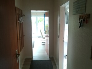A hallway with a wooden door, a mat, a chair, and a table with chairs.