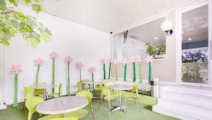 A room with round tables and yellow chairs, a green artificial grass floor, and pink flower decorations on the walls. - Stylish DBL Suite Escape W/ Free Wifi and Parking (Jakarta)