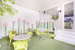 A room with round tables and yellow chairs, a green artificial grass floor, and pink flower decorations on the walls. - Stylish DBL Suite Escape W/ Free Wifi and Parking (Jakarta)