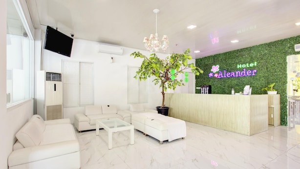 A hotel reception area with a reception desk, a large potted plant, a chandelier, and a white sofa. - Stylish DBL Suite Escape W/ Free Wifi and Parking (Jakarta)