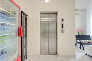 A hotel lobby with a vending machine, an elevator, and a seating area with a bench and a chair. - Stylish DBL Suite Escape W/ Free Wifi and Parking (Jakarta)
