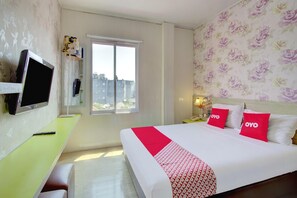 Quarto de hotel com uma cama, escrivaninha, televisão, janela e papel de parede floral.