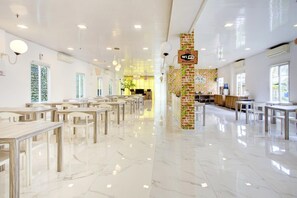Uma área de refeições ampla e bem iluminada, com mesas e cadeiras, parede de tijolos decorativa e um aviso indicando Wi-Fi gratuito.